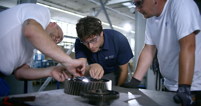 3 men working on part in workshop